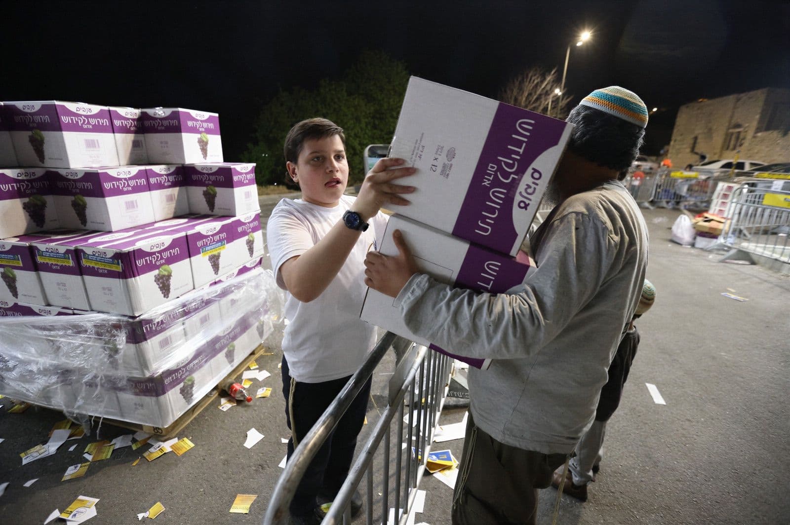 A boy receiving boxes of matzah over the barrier at a night distribution