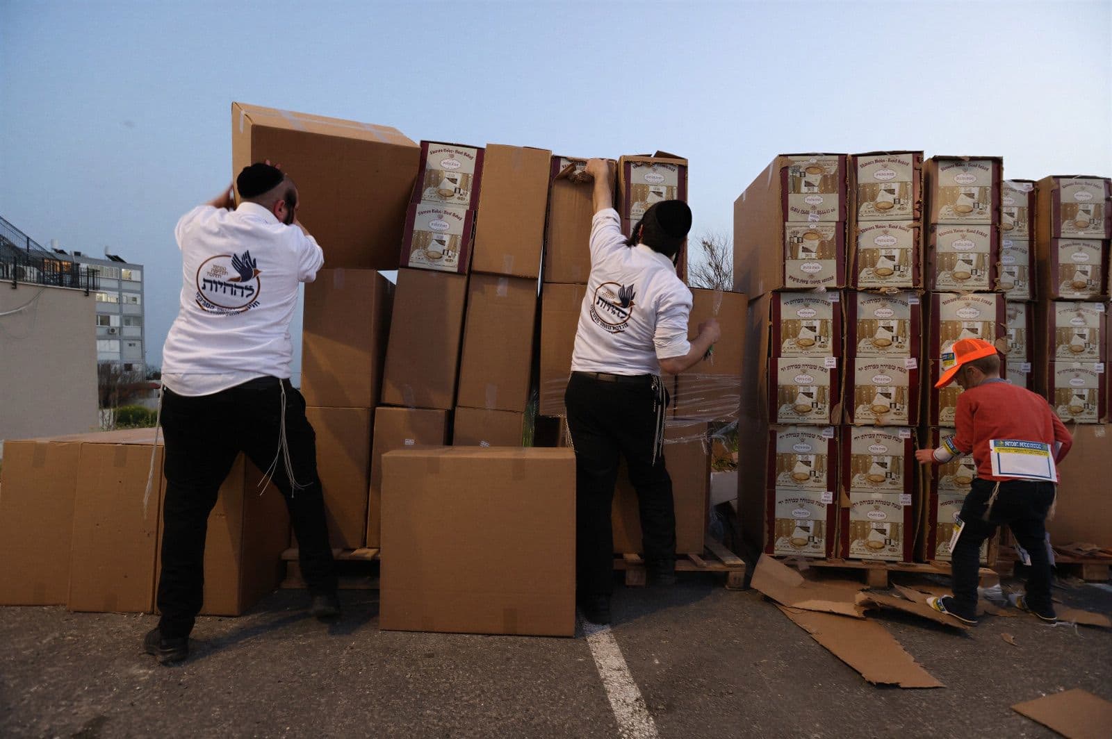 A volunteer reaching into towers of stacked boxes at a pre-Pesach distribution