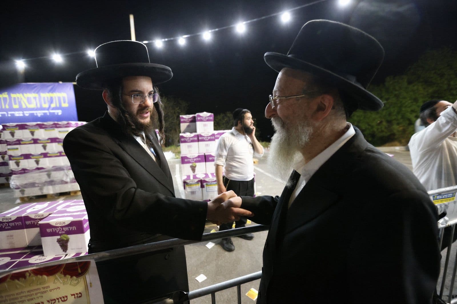 Two men shaking hands beside stacked boxes at an evening distribution