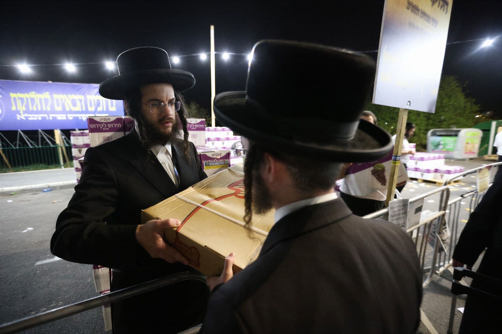 A package handed between two men under string lights at an evening distribution